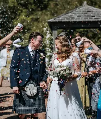 Guests throwing confetti over the bride and groom at the end of their outdoor ceremony at The Venue, Sandy Cove Hotel