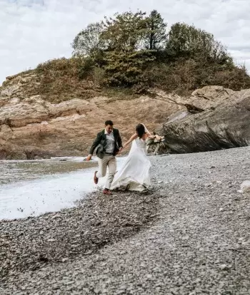 A bride and groom running from the waves on the beach near Sandy Cove Hotel after their wedding
