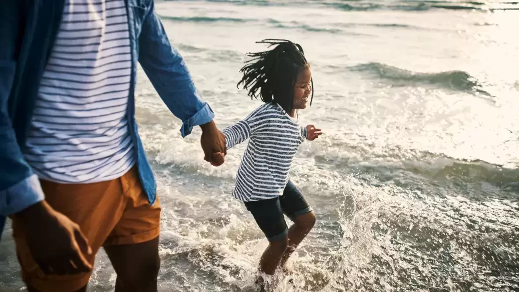 A little girl splashing in the shallows at the beach with her dad