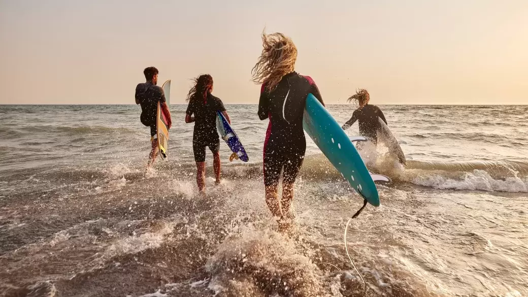 A group of surfers in wetsuits running into the sea at sunset