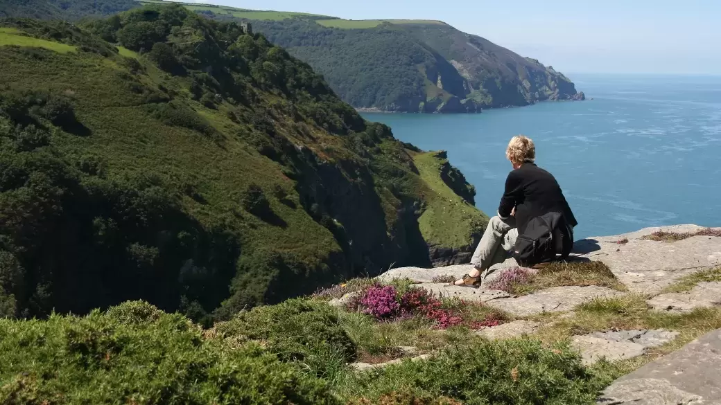 A woman sitting on top of a cliff at the Valley of Rocks overlooking the North Devon coast