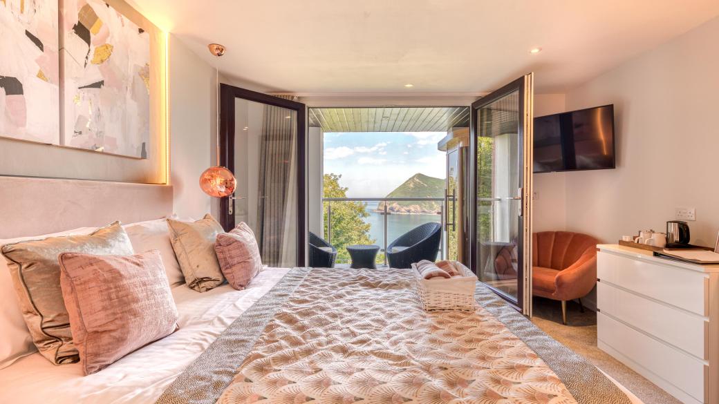 The interior of and executive sea view room with balcony at Sandy Cove Hotel showing the bed and balcony with a view over the bay