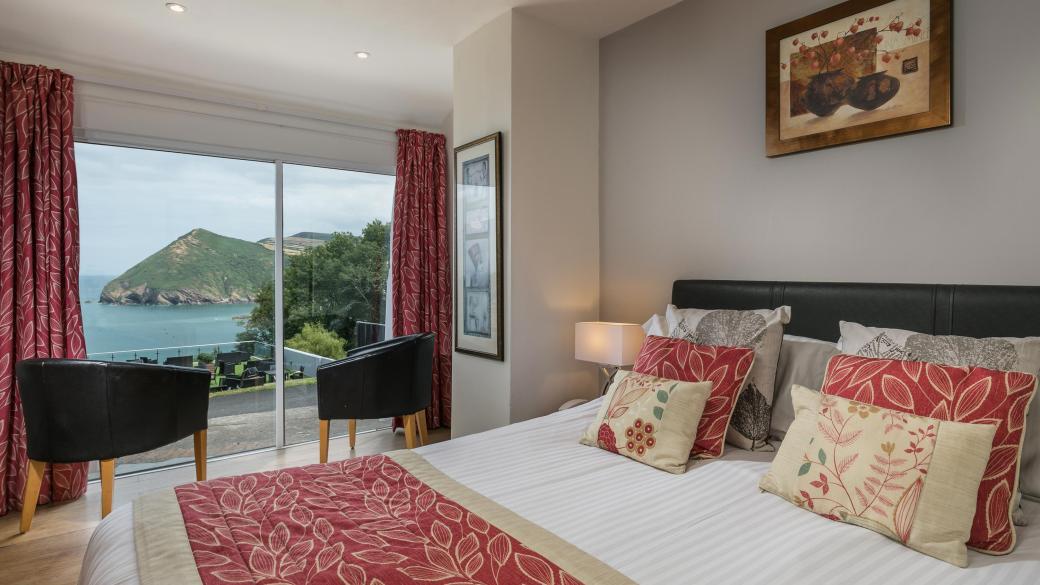 The bed and seating area with a view over the bay in one of the Standard Rooms at Sandy Cove Hotel