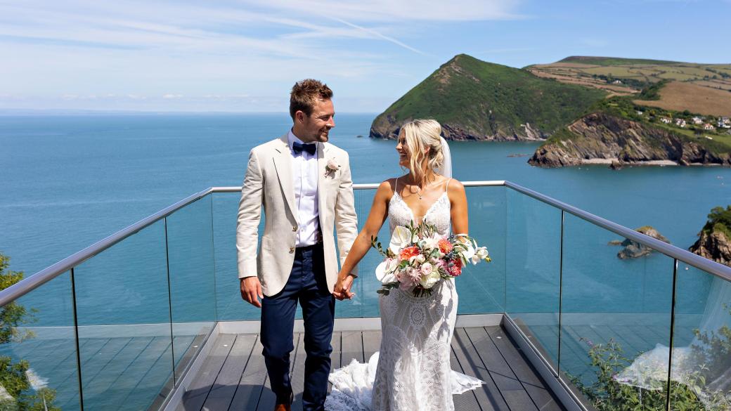 A bride and groom standing on the platform overlooking the bay on their Wedding day at Sandy Cove Hotel's The Venue
