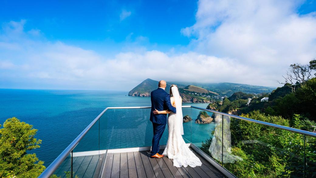 A bride and groom standing on the platform at The Venue, Sandy Cove, looking at the view of the bay