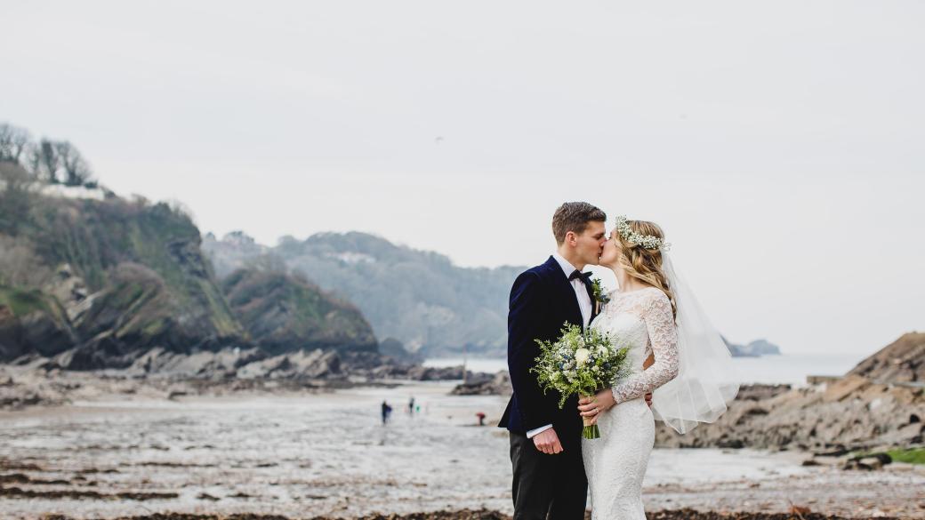 A bride and groom kissing on Broadsands beach near Sandy Cove Hotel on their wedding day