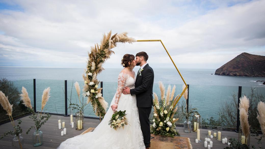 A bride and groom sharing a kiss on the deck of the Venue overlooking the bay