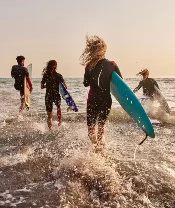 A group of surfers in wetsuits running into the sea at sunset