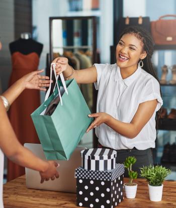 A smiling cashier handing a bag to a customer in a clothing shop