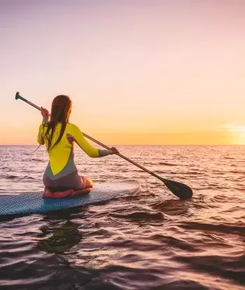 A paddleboarder kneeling on her board on calm seas at sunset