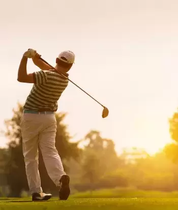 A golfer teeing off on a summer evening