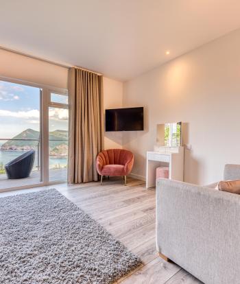 The interior of a luxury sea view room at Sandy Cove Hotel showing the seating area, balcony and view over the sea