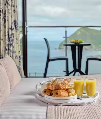 A breakfast tray with food and juice sitting on the bed in one of Sandy Cove Hotel's classic sea view with balcony rooms