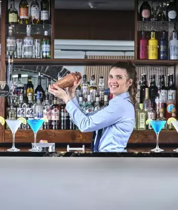A bartender making drinks with a cocktail shaker in the bar at Sandy Cove Hotel