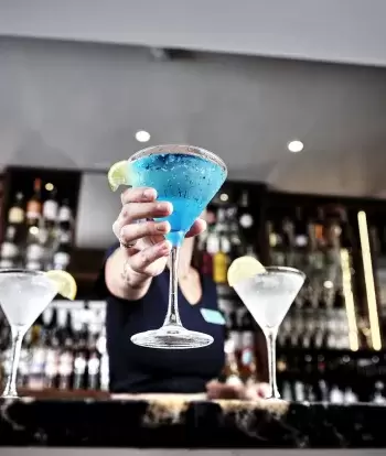 A bar tender at Sandy Cove Hotel making colourful cocktails at the bar