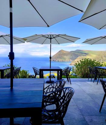 Tables with parasols on the Terrace at Sandy Cove Hotel and a view of the bay in the distance
