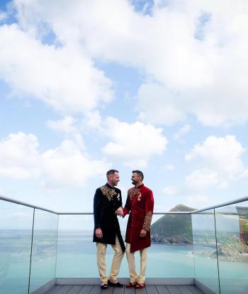 Two grooms standing at the end of the platform at Sandy Cove Hotel on their wedding day with a view of the bay in the background