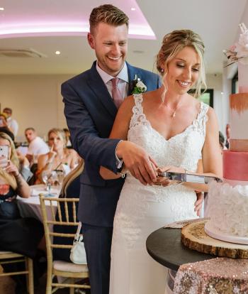 A bride and groom cutting the cake at their wedding at The Venue, Sandy Cove Hotel
