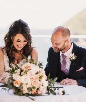 A bride and groom signing their wedding licence on the platform at The Venue, Sandy Cove Hotel, overlooking the bay