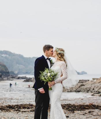 A bride and groom kissing on Broadsands beach near Sandy Cove Hotel on their wedding day