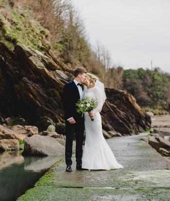 A bride and groom kissing on the beach near Sandy Cove Hotel after their wedding