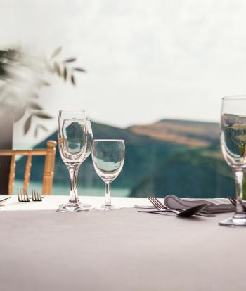 A table in The Venue at Sandy Cove set with cutlery and wine glasses and a view of the bay behind