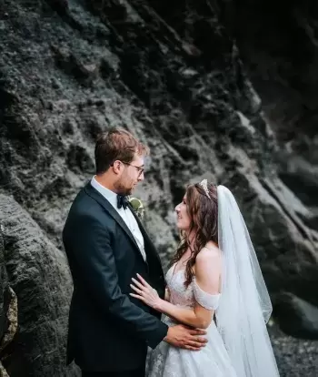 A bride and groom looking at each other as they stand on the beach by Sandy Cove Hotel on their wedding day