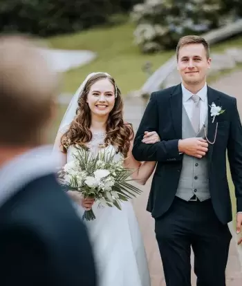 A bride being walked down the path towards her outdoor wedding ceremony at The Venue, Sandy Cove Hotel