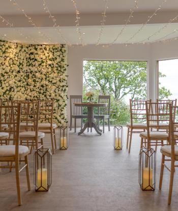A wedding table with chairs on either side of the aisle in the ceremony room at Sandy Cove Hotel