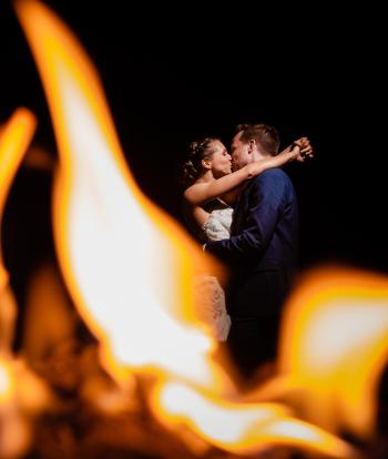 Newly married couple embrace by fire
