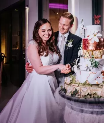 A smiling bride and groom cutting their wedding cake in The Venue at Sandy Cove Hotel