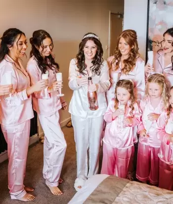 A bride wearing pyjamas celebrating her wedding day at Sandy Cove Hotel by sharing a bottle of Prosecco with her bridesmaids
