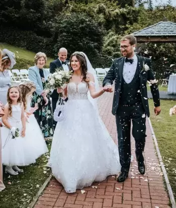 Guests throwing confetti over a bride and groom after their outdoor wedding ceremony at The Venue, Sandy Cove Hotel