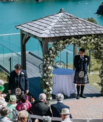 A groom standing under the arch outside The Venue at Sandy Cove Hotel waiting for his bride to arrive