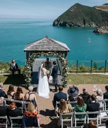 A bride and groom standing in front of their guests in the outdoor ceremony area overlooking the bay at Sandy Cove Hotel