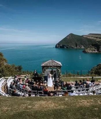An outdoor wedding ceremony in front of The Venue at Sandy Cove Hotel with a view over the bay