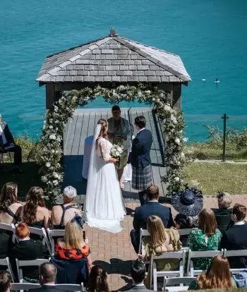 A couple getting married at an outdoor ceremony with guests overlooking the bay at Sandy Cove Hotel