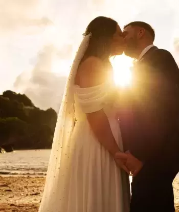 A bride and groom kissing on the beach by Sandy Cove Hotel on their wedding day