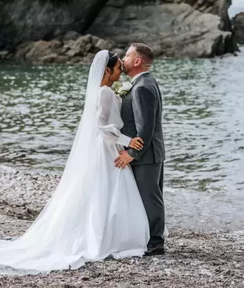 A groom kissing his bride by the sea on the beach by Sandy Cove Hotel