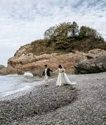 A bride and groom nearing the sea on the beach by Sandy Cove Hotel