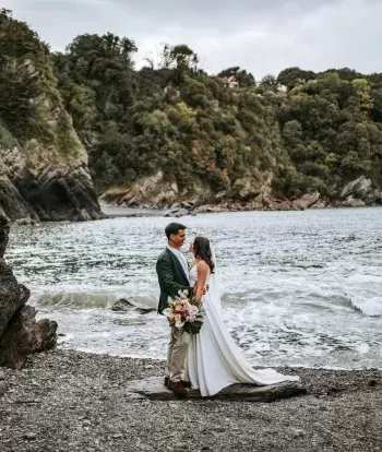 A newly-wed couple standing on the beach by Sandy Cove Hotel with the sea behind them