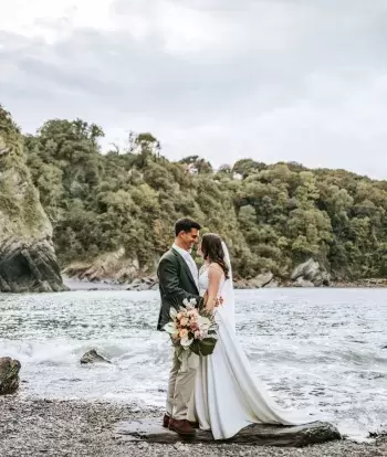 A newly-wed couple standing on the beach near Sandy Cove Hotel with the sea behind them