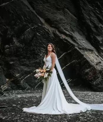 A happy bride standing alone on the beach near Sandy Cove Hotel after her wedding