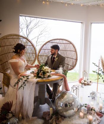 Bride and groom sat inside at table with the view behind them