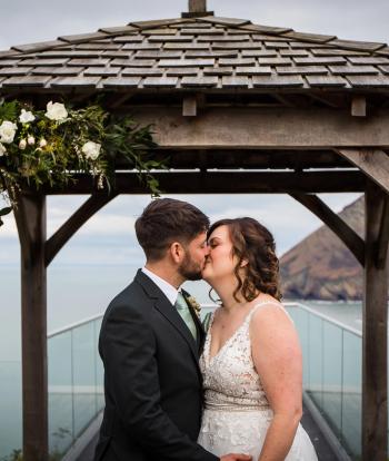 Bride and groom standing outside by the arbour with beautiful view behind them
