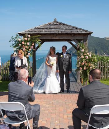 Bride and groom standing by the arbour with beautiful view behind them