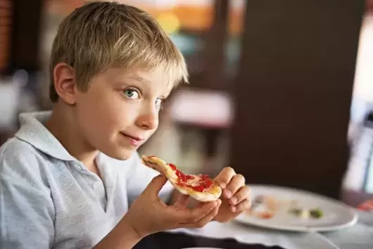 A young boy holding a slice of pizza about to take a bite