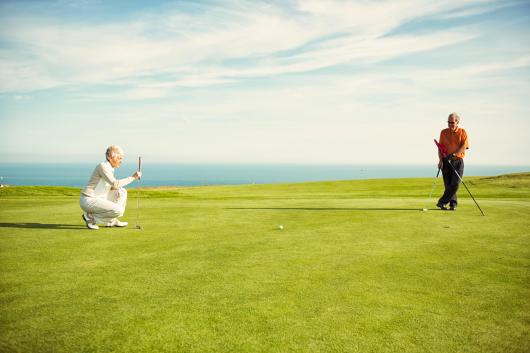 Couple playing golf on green in North Devon with blue sea in background
