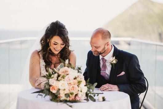 A bride and groom signing their wedding licence on the platform at The Venue, Sandy Cove Hotel, overlooking the bay