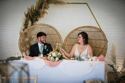 A bride and groom with wine glasses sat at a table decorated with winter decorations in The Venue, Sandy Cove Hotel